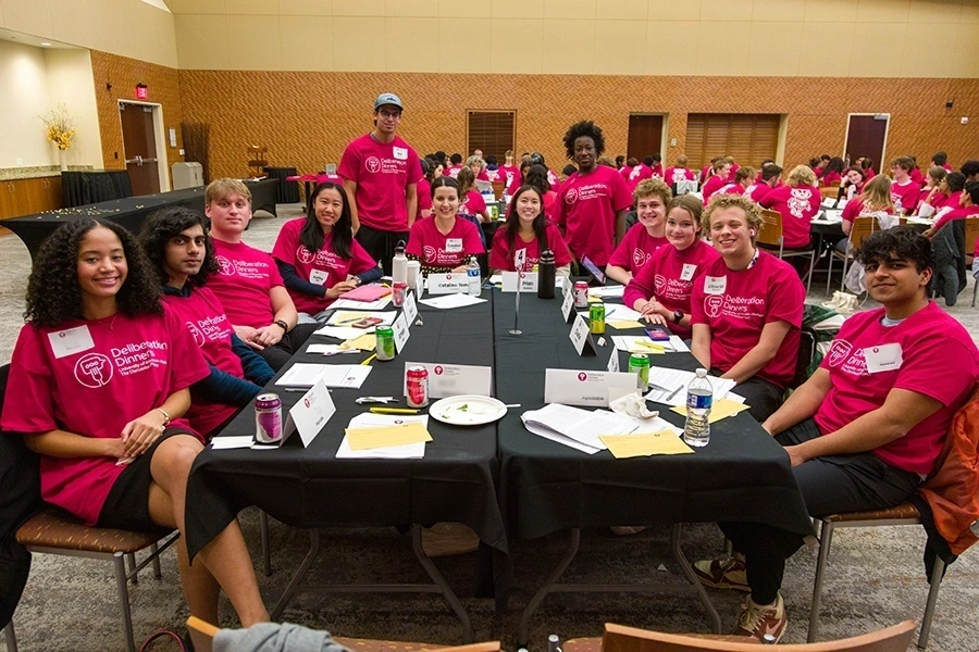 Group of students sitting around a table and wearing red shirts.