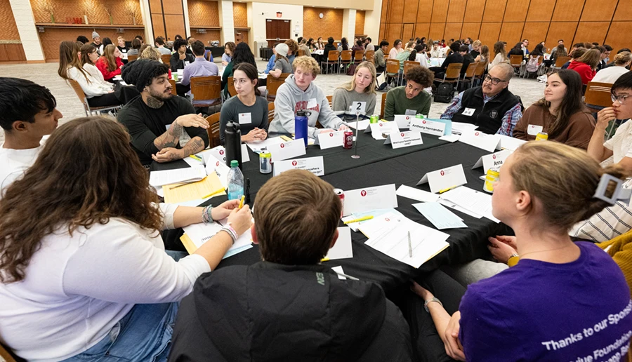 A large group having a discussion at a table in a large room with other groups at tables.