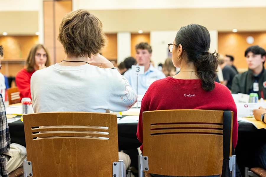 View from behind of two students sitting in wooden chairs at a table.